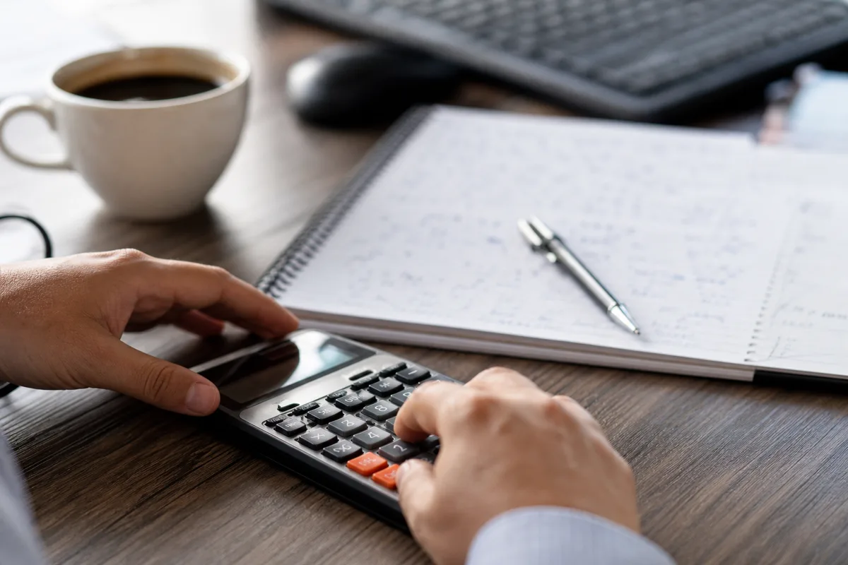 Mains calculant des montants sur une calculatrice à côté d&rsquo;un carnet de chiffres